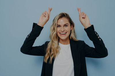 Portrait of young woman with arms raised standing against white background