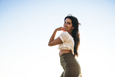 Young latina woman smiling by the ocean at golden hour in summertime