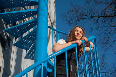 Low angle view of woman on railing against blue sky