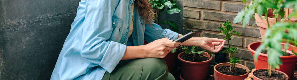 Woman checking plants of urban garden on terrace while holding digital tablet in hand