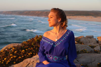 Woman sitting on rock looking at sea shore against sky