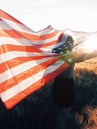 Woman holding us flag against sunset 