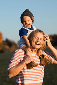 Happy mother carrying son on shoulders while standing in park