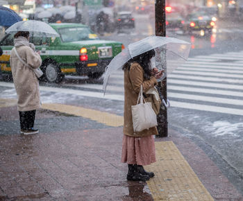 Full length of woman walking on wet street during rainy season