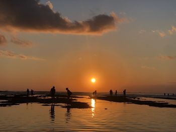 Silhouette people on beach against sky during sunset