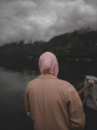 Rear view of woman standing by lake against sky