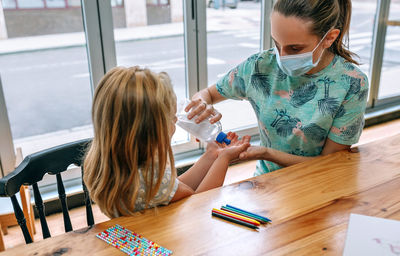 Woman and daughter using sanitizer sitting on table