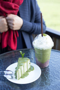 Midsection of person holding ice cream with drink on table