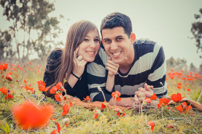 Portrait of happy couple lying amidst poppy flowers on field