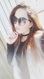 Beautiful young woman with long brown hair wearing sunglasses at home