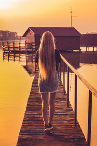 Rear view of woman standing on pier against sky during sunset