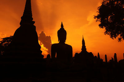 Silhouette buddhist temple against dramatic sky at sunset