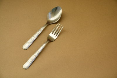 High angle view of fork with spoon on brown background