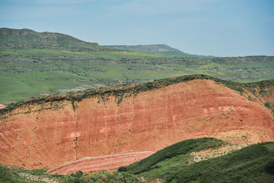 A breathtaking ethereal landscape with vibrant multi-colored red hills under a cloudy sky. 