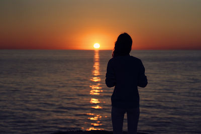 Silhouette man looking at sea against sky during sunset