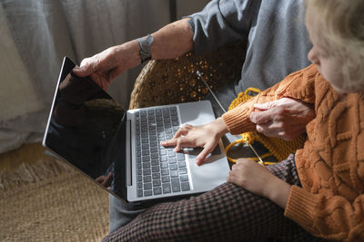 Girl using laptop sitting by grandmother on chair