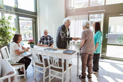 Senior man and woman shaking hands near friends and nurse at nursing home