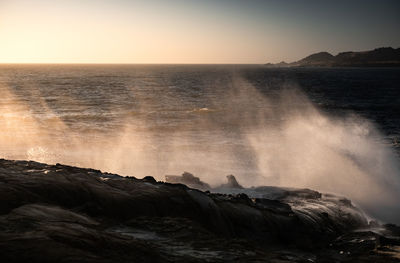 Waves splashing on rocks at shore against sky