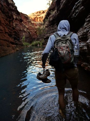 Rear view of young man with backpack standing in river amidst mountains