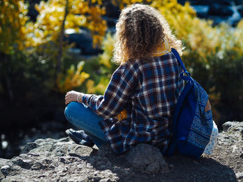 Young curly woman traveller in yoga pose doin meditation on a hill in autumn forest