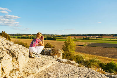 Woman sitting on rock against sky