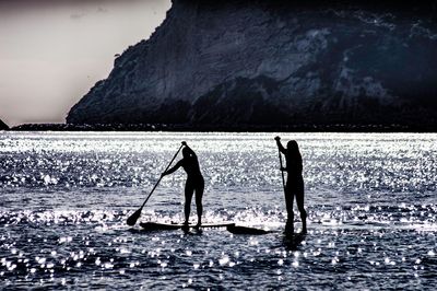 Silhouette people standing in sea against sky