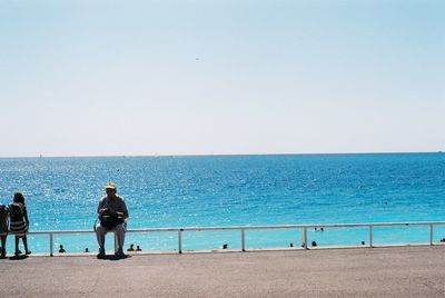 Rear view of men on beach against clear sky