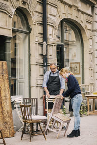 Retailer assisting customer in choosing chair outside antique shop