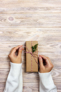 High angle view of woman tying ribbon on gift over table