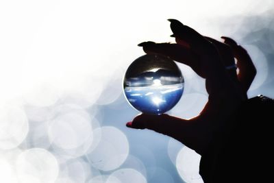 Silhouette person holding crystal ball against sky