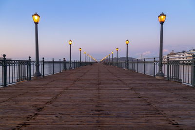 Low angle view of illuminated lamp posts on pier seven against clear sky at dusk