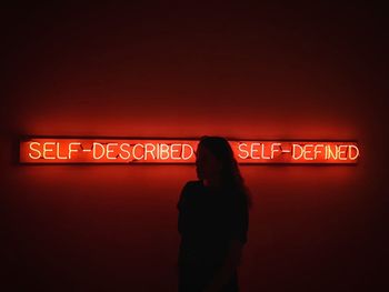 Rear view of man standing against illuminated sign at night