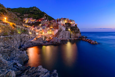 Scenic view of sea by illuminated buildings against sky