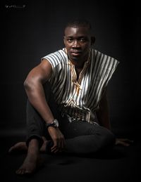 Portrait of young man sitting against black background