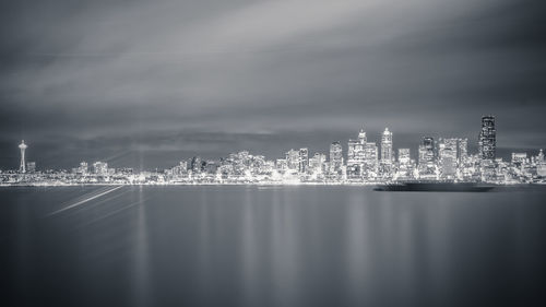 Illuminated city by sea against sky at night