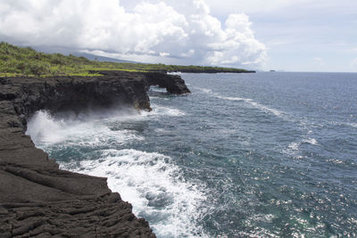 Volcanic coastal cliffs with blue waves breaking during sunny day