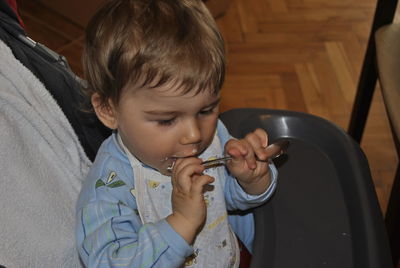 Close-up of cute boy with messy mouth holding spoon on baby stroller at home