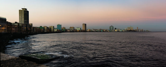 Sea by buildings against sky during sunset