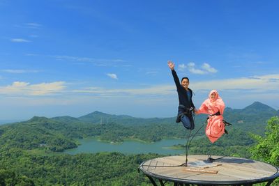 Woman with arms raised on mountain against sky