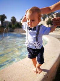 Full length of cute baby boy walking on retaining wall by fountain in city