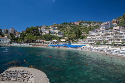 Scenic view of beach by buildings against clear blue sky