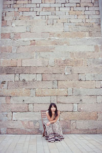 Full length of woman sitting on brick wall