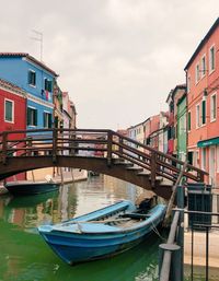 Boats moored in canal by buildings against sky
