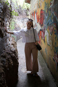 Full length portrait of young woman standing against graffiti wall