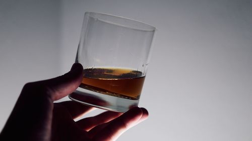 Close-up of hand holding drink against white background
