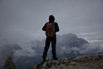 Rear view of man standing on rock against sky