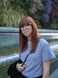 Portrait of mid adult woman standing on footpath by wet road