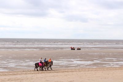 People riding horse on beach against sky