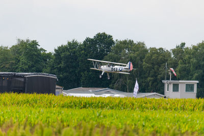 Airplane flying over grassy field against sky