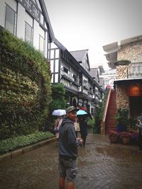 Rear view of man standing amidst buildings in city during rainy season